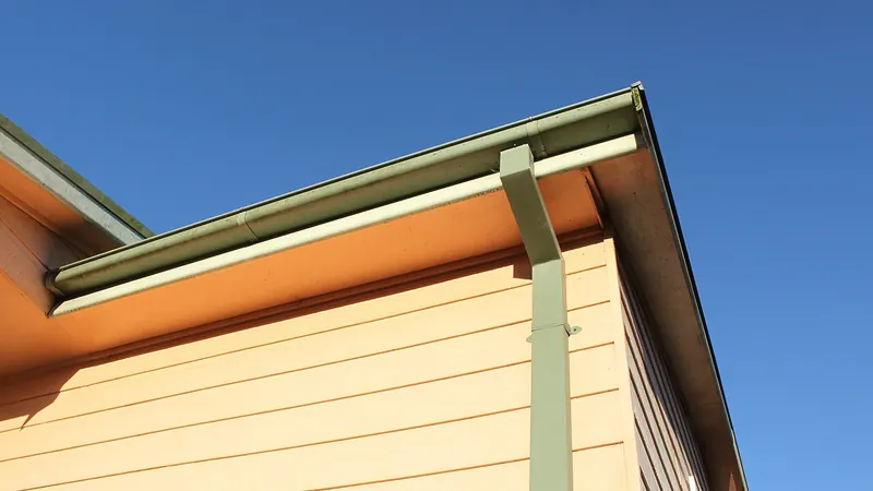 Gutter and downspout along a roof edge against a blue sky