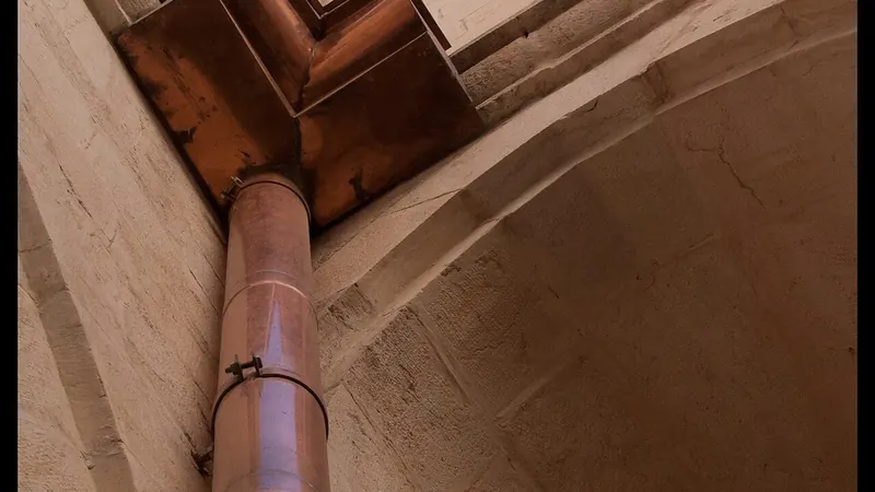 Copper half-round gutter with a round downspout on a historic brick wall