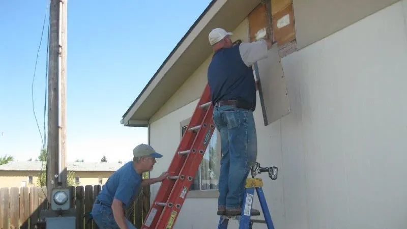 Workers on ladders installing siding on a house wall