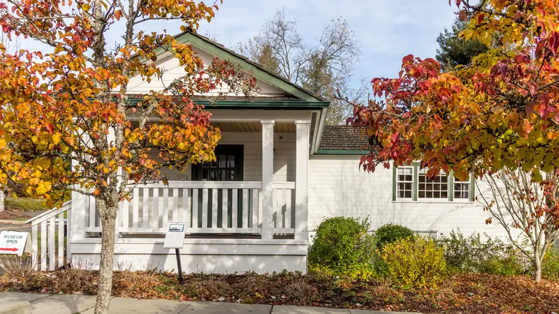 White house with a porch beneath red and gold autumn trees