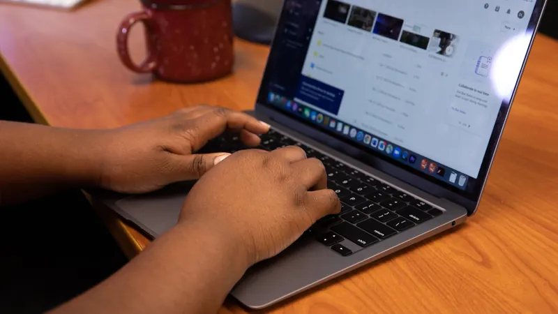 Hands typing on a laptop on a wooden table next to a mug